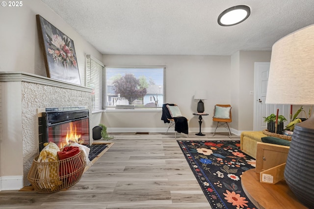 sitting room with a textured ceiling, a tiled fireplace, wood finished floors, and baseboards