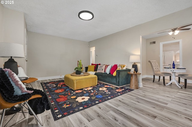 living room with wood finished floors, a ceiling fan, a textured ceiling, and baseboards