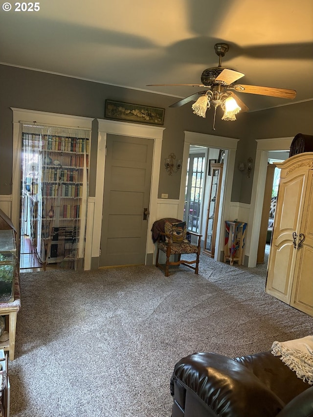 living area featuring a wainscoted wall, ceiling fan, carpet flooring, and a decorative wall