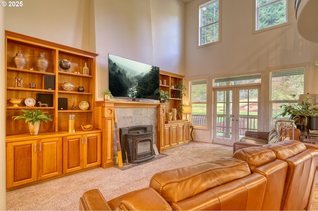 living room featuring a wood stove, french doors, a towering ceiling, and light colored carpet