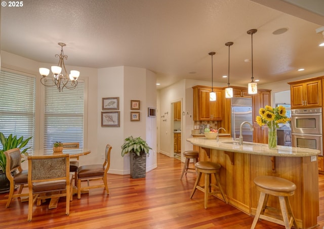 kitchen with light stone counters, appliances with stainless steel finishes, a breakfast bar, light wood-style floors, and a sink