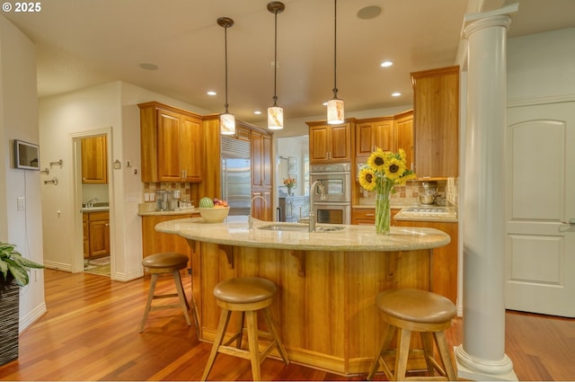 kitchen with a sink, appliances with stainless steel finishes, decorative backsplash, light wood finished floors, and ornate columns