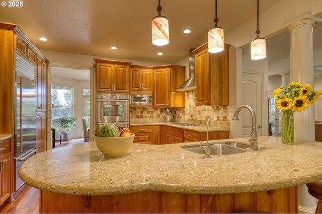 kitchen with decorative backsplash, wall chimney exhaust hood, a kitchen breakfast bar, built in appliances, and a sink