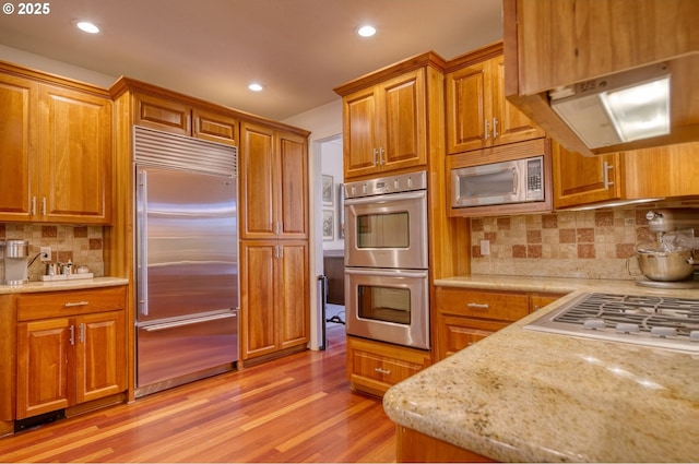 kitchen featuring built in appliances, light stone counters, light wood-style flooring, and brown cabinets