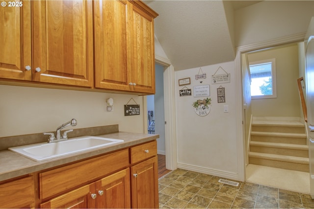 kitchen featuring brown cabinets, light countertops, visible vents, a sink, and baseboards