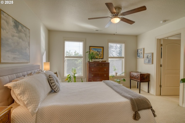 bedroom featuring light carpet, a textured ceiling, visible vents, and a ceiling fan