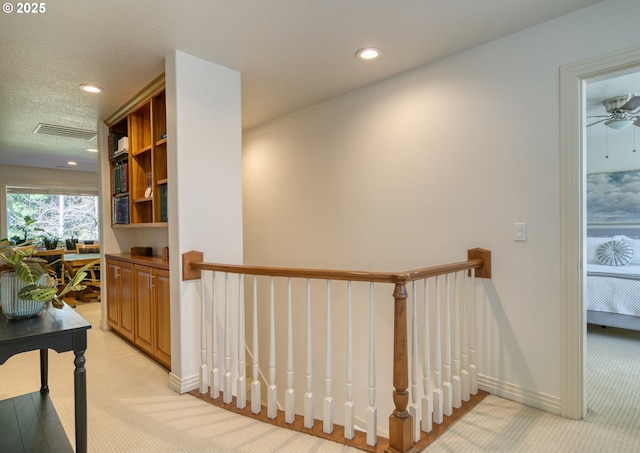 hall with baseboards, visible vents, a textured ceiling, and an upstairs landing