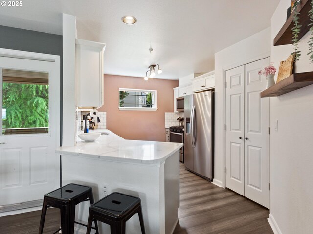 12130 NE Fremont St Unit 4, Portland, OR 97220 - kitchen featuring stainless steel appliances, white cabinetry, a peninsula, backsplash, and dark wood-type flooring