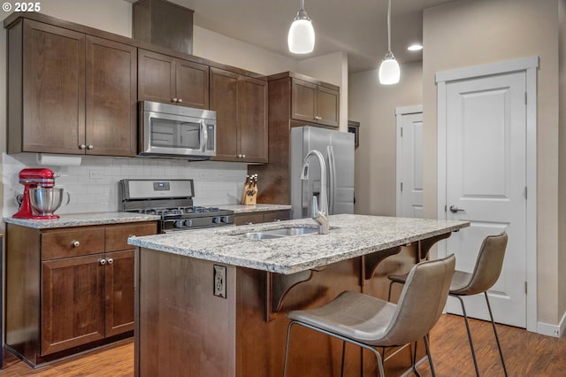 kitchen featuring appliances with stainless steel finishes, hanging light fixtures, a kitchen breakfast bar, light stone countertops, and a center island with sink