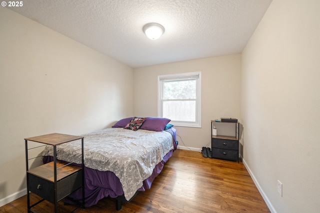 bedroom featuring a textured ceiling, baseboards, and wood finished floors