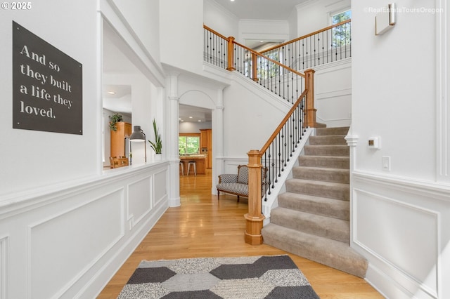 foyer featuring crown molding, light wood-type flooring, plenty of natural light, and a decorative wall