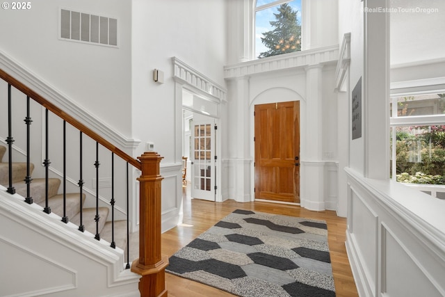 foyer featuring light wood finished floors, a towering ceiling, visible vents, and a decorative wall