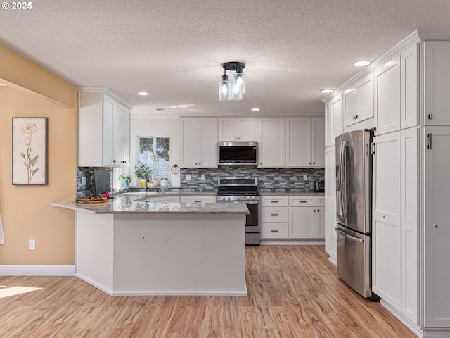 kitchen with a peninsula, white cabinetry, light wood-style flooring, appliances with stainless steel finishes, and backsplash
