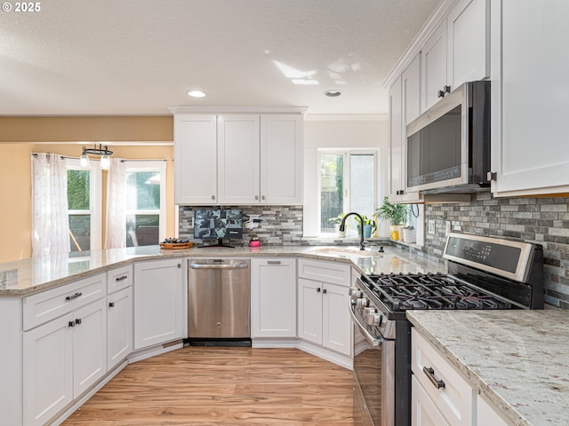 kitchen with appliances with stainless steel finishes, tasteful backsplash, a sink, white cabinets, and a peninsula