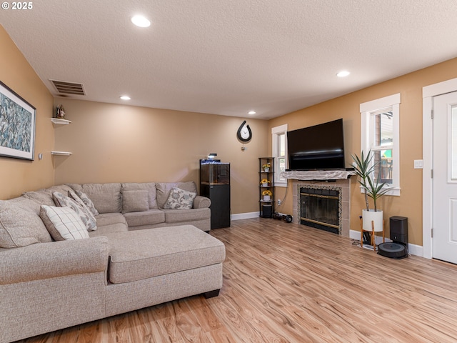 living room featuring visible vents, a textured ceiling, baseboards, and light wood-style floors
