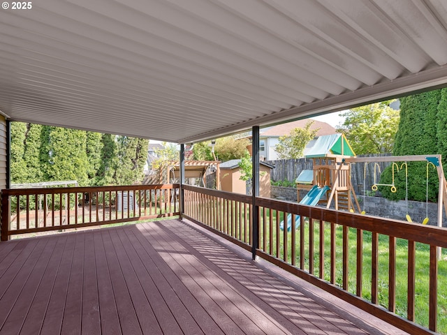 wooden deck featuring a fenced backyard, a storage unit, a playground, a lawn, and an outbuilding