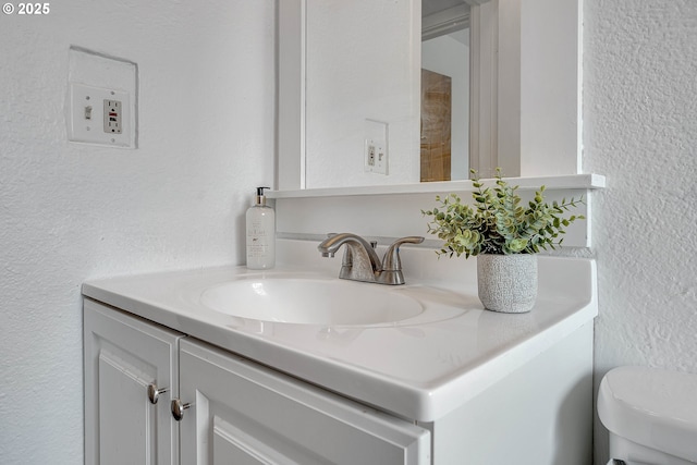 half bath with toilet, a textured wall, and vanity