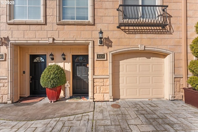 entrance to property with decorative driveway, stone siding, and an attached garage