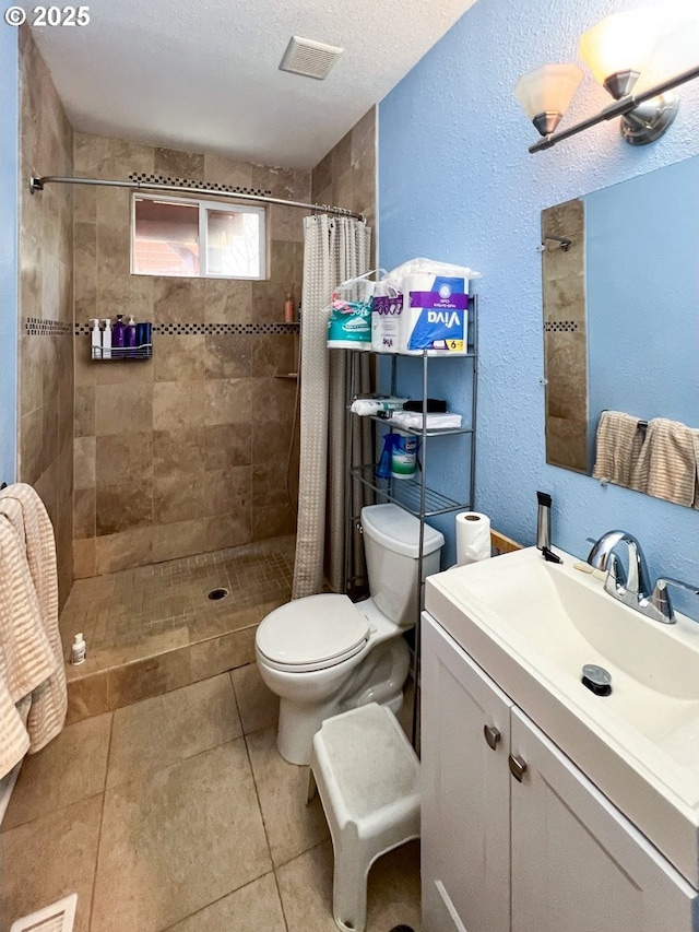 bathroom with tiled shower, a textured wall, toilet, tile patterned floors, and vanity