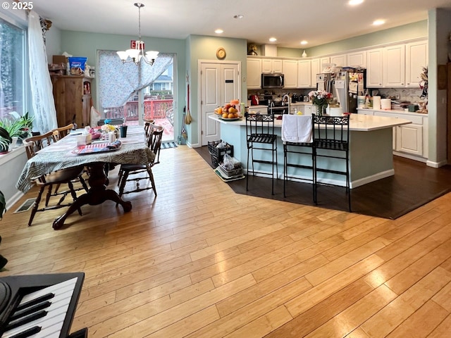 kitchen featuring stainless steel appliances, white cabinets, light countertops, hanging light fixtures, and an island with sink