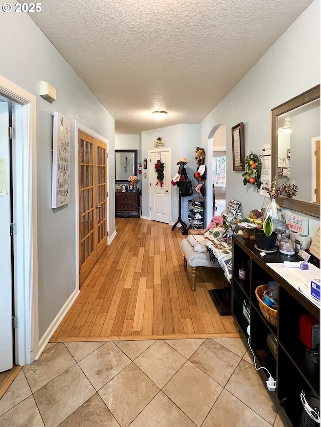 hallway with arched walkways, a textured ceiling, and light tile patterned floors