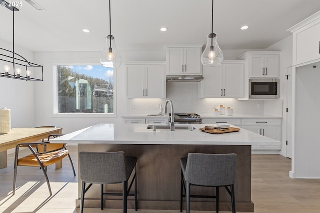 kitchen featuring built in microwave, sink, white cabinetry, pendant lighting, and a kitchen island with sink