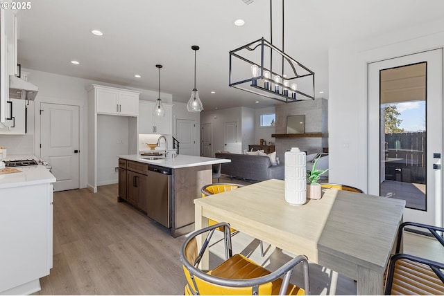 kitchen featuring white cabinetry, dishwasher, sink, hanging light fixtures, and a kitchen island with sink