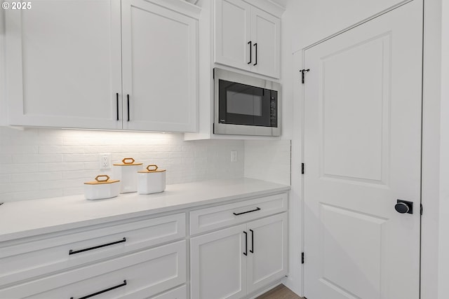 kitchen featuring built in microwave, backsplash, and white cabinets