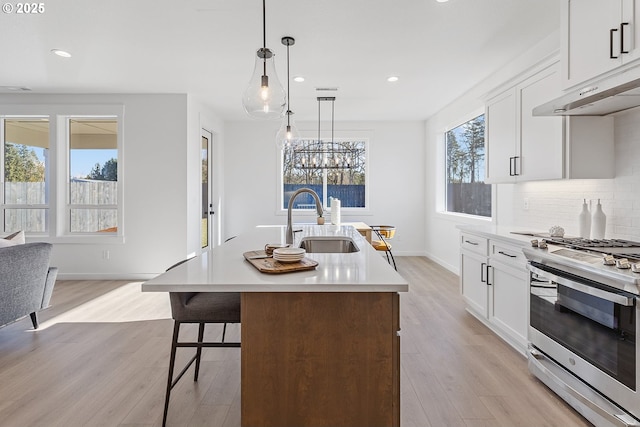 kitchen with decorative light fixtures, an island with sink, sink, white cabinets, and gas range