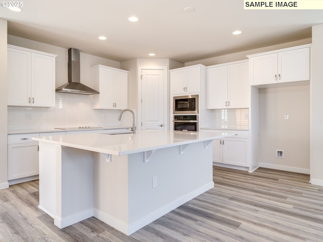 kitchen featuring built in microwave, an island with sink, white cabinets, oven, and wall chimney range hood