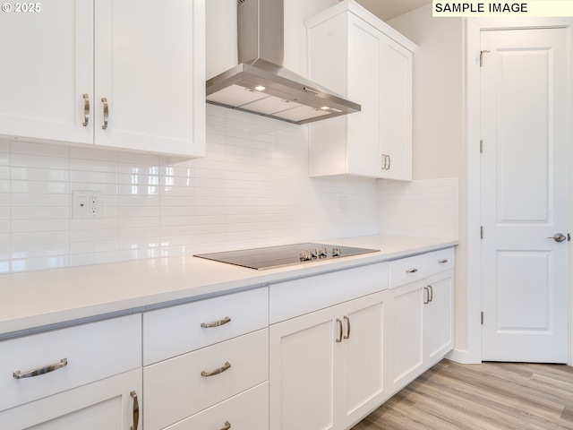 kitchen featuring white cabinetry, wall chimney range hood, light hardwood / wood-style floors, and black electric stovetop