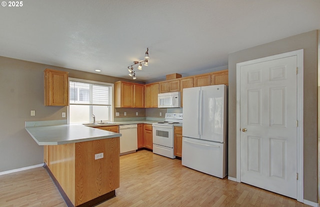 kitchen featuring a peninsula, white appliances, a sink, light countertops, and light wood finished floors