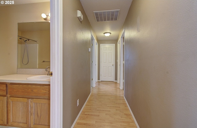 hallway featuring light wood-type flooring, visible vents, a sink, and baseboards