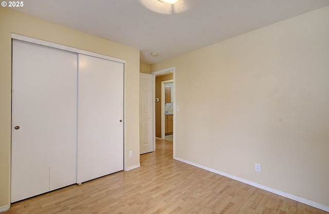 unfurnished bedroom featuring light wood-style flooring, baseboards, and a closet