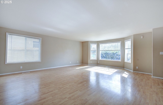 spare room with light wood-type flooring, visible vents, and baseboards