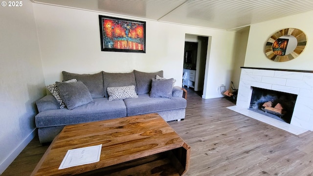 living area with baseboards, a tile fireplace, and wood finished floors