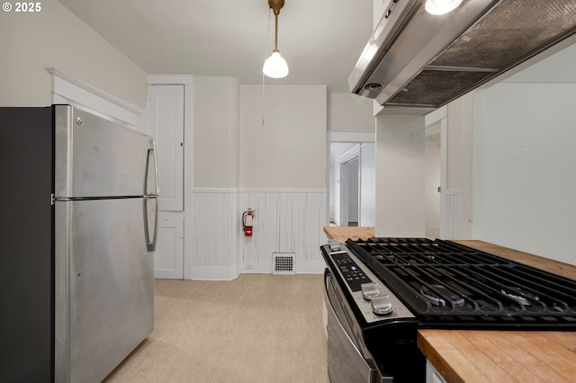kitchen with freestanding refrigerator, butcher block countertops, a wainscoted wall, range with gas cooktop, and light carpet