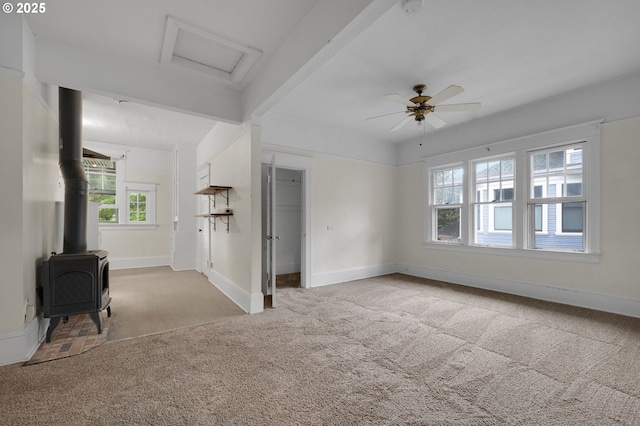 unfurnished bedroom with a wood stove, attic access, carpet flooring, and multiple windows