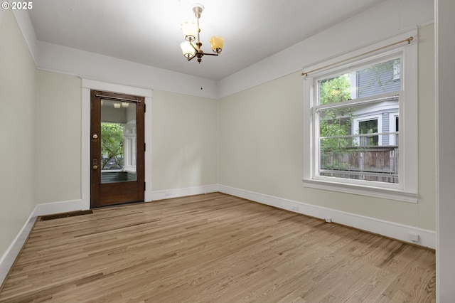 empty room with baseboards, a wealth of natural light, light wood finished floors, and an inviting chandelier