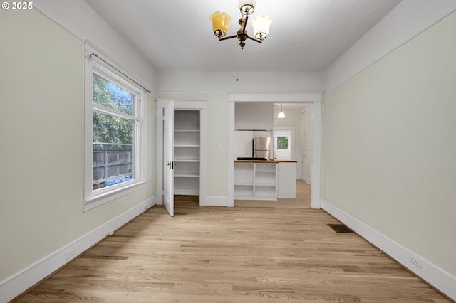 unfurnished dining area featuring baseboards, light wood-style floors, a chandelier, and visible vents