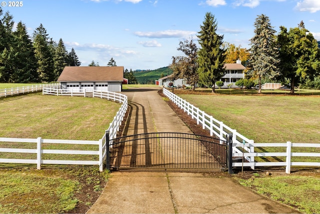 view of yard with concrete driveway, an outdoor structure, a rural view, and a gate