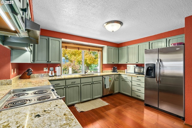 kitchen featuring stainless steel appliances, green cabinetry, a sink, dark wood-style flooring, and a textured ceiling
