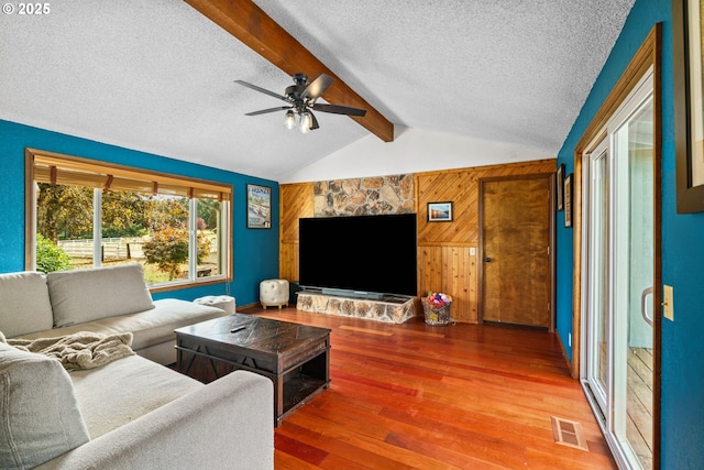 living room featuring a textured ceiling, wooden walls, wood finished floors, and ceiling fan
