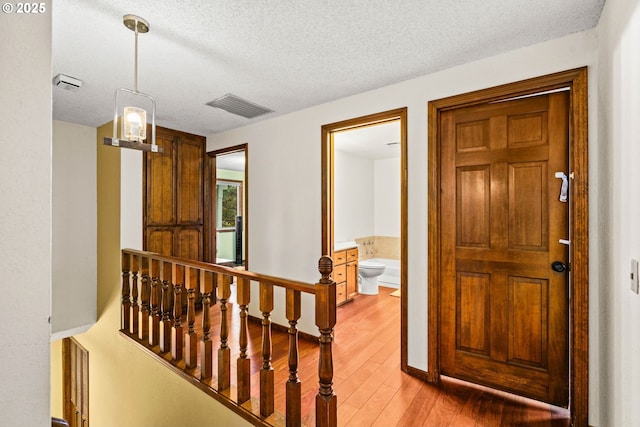 corridor with a textured ceiling, light wood-style flooring, an upstairs landing, and baseboards