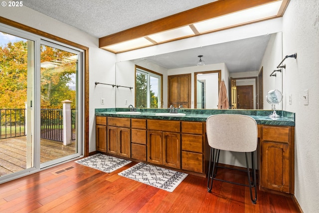 full bathroom with a textured wall, double vanity, hardwood / wood-style flooring, a textured ceiling, and baseboards