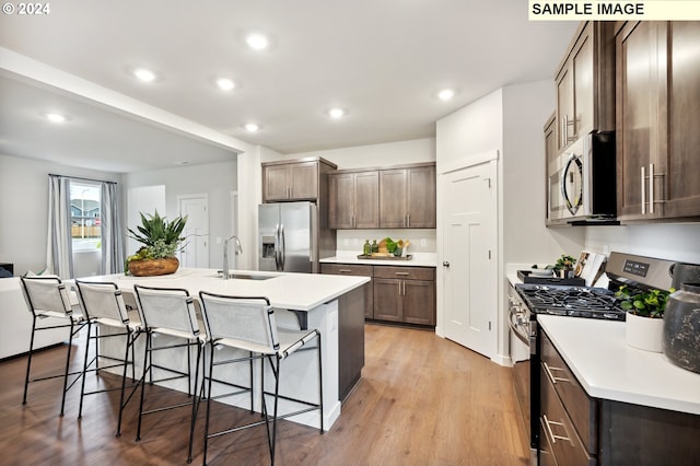 kitchen featuring appliances with stainless steel finishes, light hardwood / wood-style floors, sink, a breakfast bar, and a center island with sink