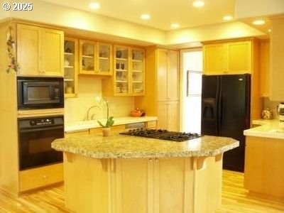 9587 NW Caxton Ln, Portland, OR 97229 - kitchen with black appliances, light wood-style floors, a center island, glass insert cabinets, and a kitchen breakfast bar