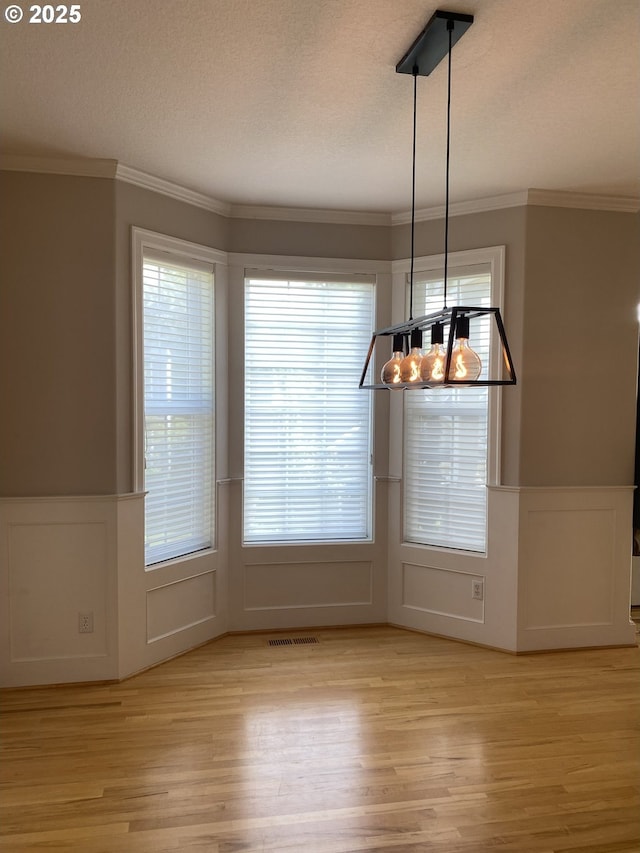 9587 NW Caxton Ln, Portland, OR 97229 - unfurnished dining area with a wainscoted wall, a decorative wall, light wood finished floors, crown molding, and a textured ceiling