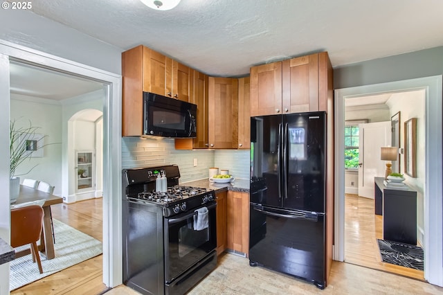 5536 N Delaware Ave, Portland, OR 97217 - kitchen featuring black appliances, backsplash, light wood-style floors, arched walkways, and brown cabinets