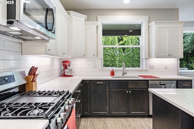 kitchen featuring appliances with stainless steel finishes, a sink, white cabinetry, light wood-style flooring, and recessed lighting